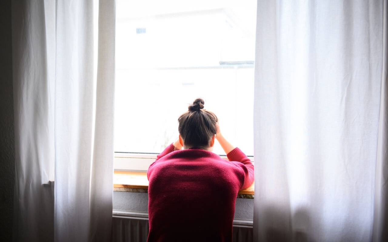 Eine Frau sitzt mit Kopf in den Händen am Fenster