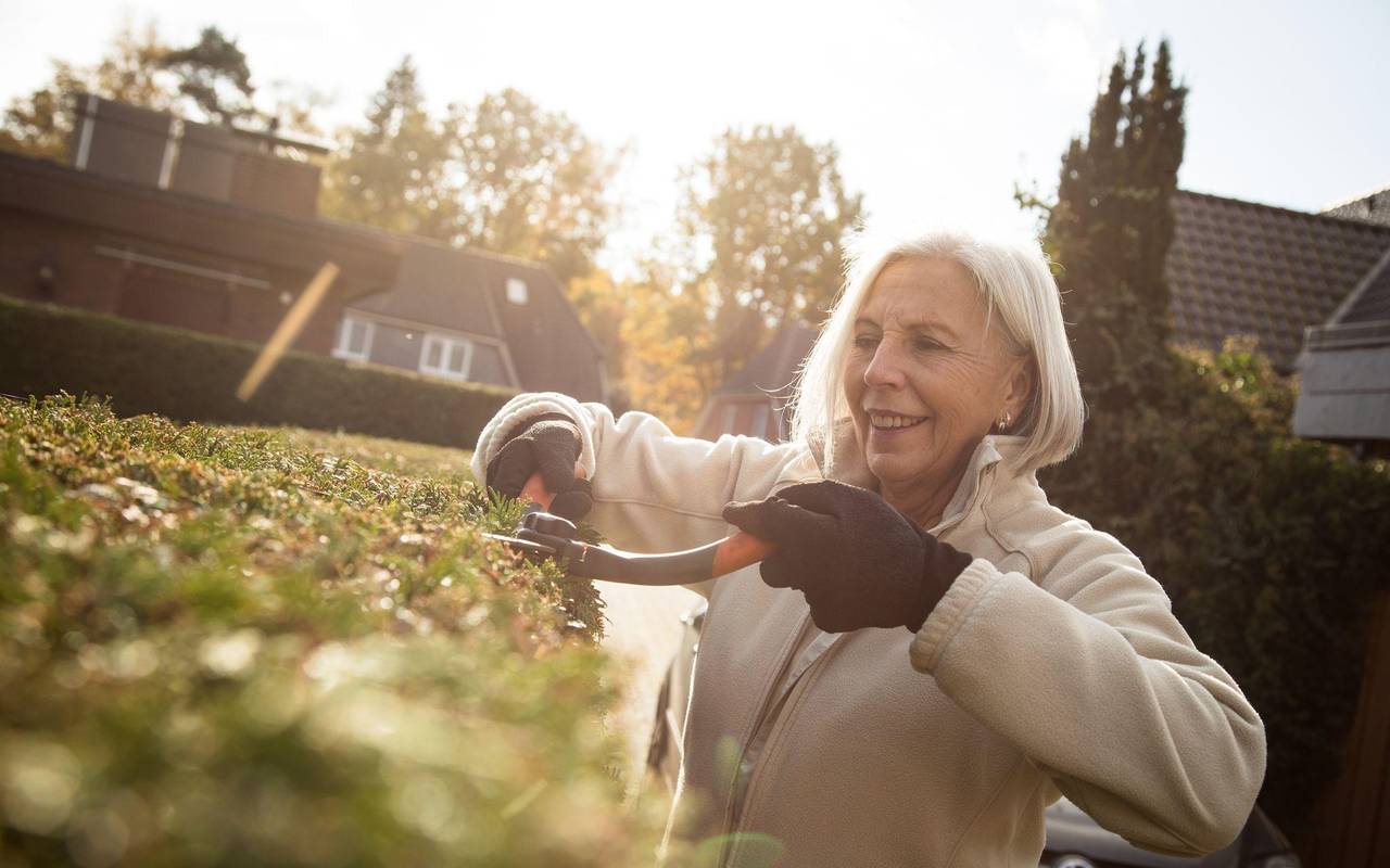 Eine ältere Dame schneidet eine Hecke