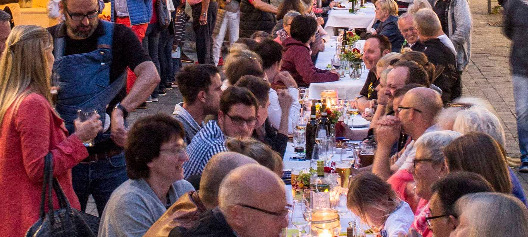 Auf dem Bild ist die lange Tafel in der Altstadt von Arnsberg zu sehen, an dem die Leute gemeinsam verschiedenste Gerichte verspeisen.