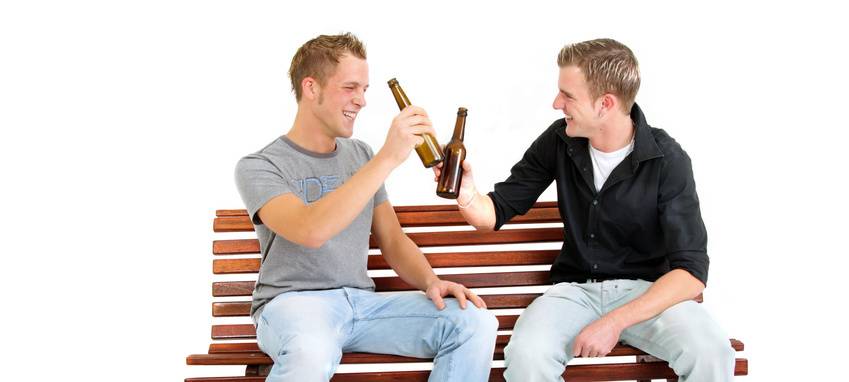 Zwei Männer sitzen auf einer Bank und stoßen mit Bierflaschen an.