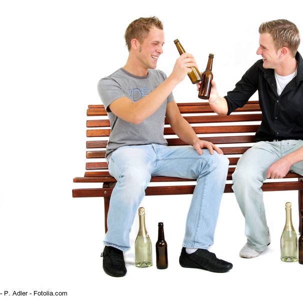 Zwei Männer sitzen auf einer Bank und stoßen mit Bierflaschen an.