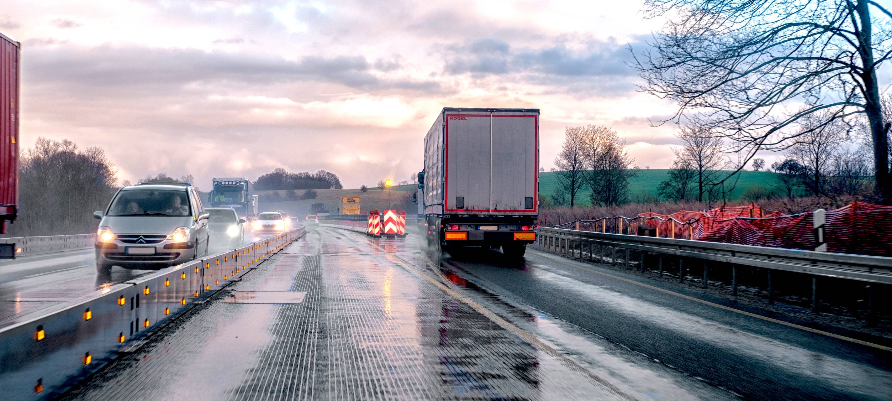 Eine verengte Fahrspur auf einer deutschen Autobahn, die ein nass-kaltes Wetter zeigt, bei dem im Gegenverkehr die Scheinwerfer der Autos erkennbar sind.