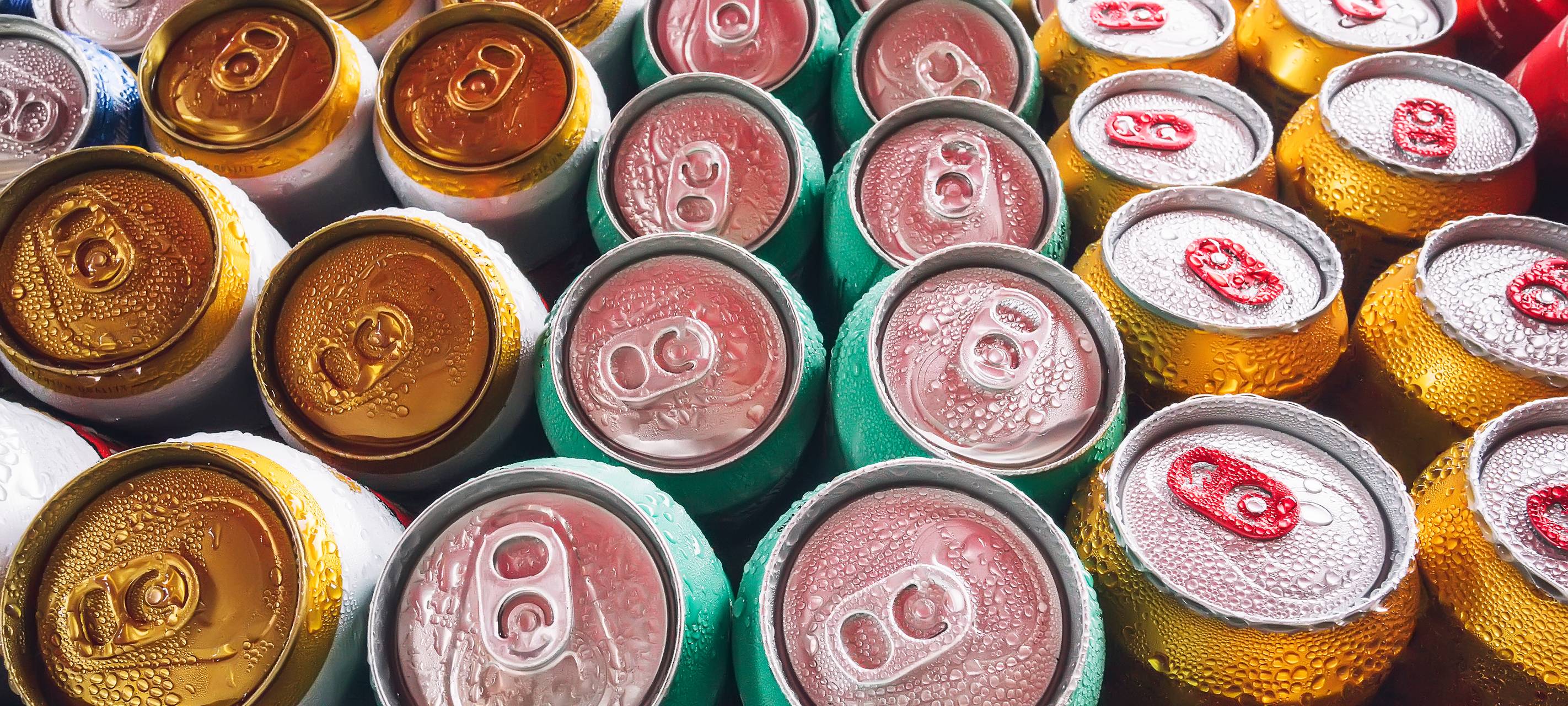 Metalldosen, gefüllt mit Bier auf Eiswürfeln im Minikühlschrank, Nahaufnahme. Viele Aluminiumdosen im Eis im offenen Kühlschrank. Tropfen Wasser auf eine kalte Getränkedose.