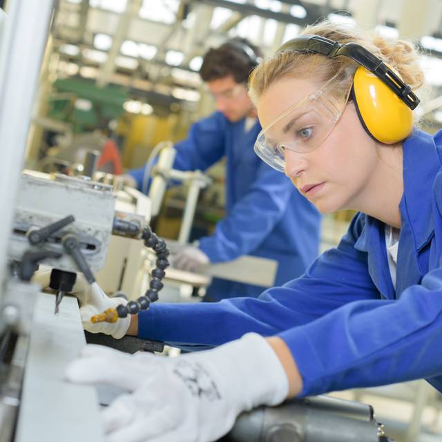 Eine Frau arbeitet an einer industriellen Fertigungsanlage (Symbolbild).