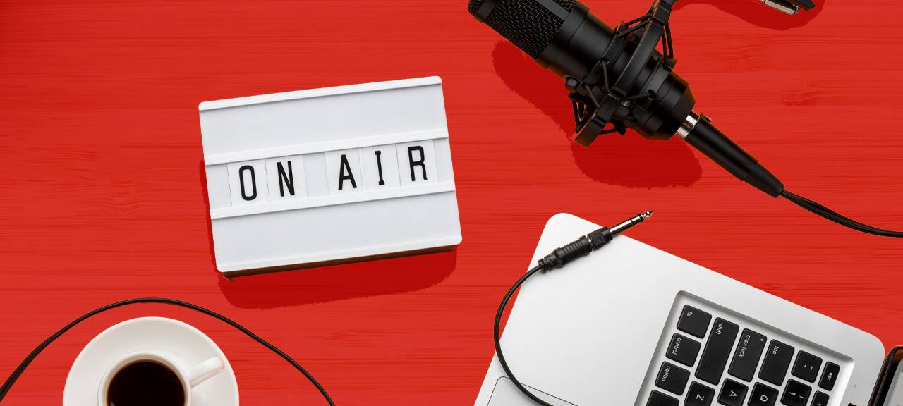 Foto von einem Laptop, Mikrofon, "On Air"-Schild und einer Tasse Kaffee