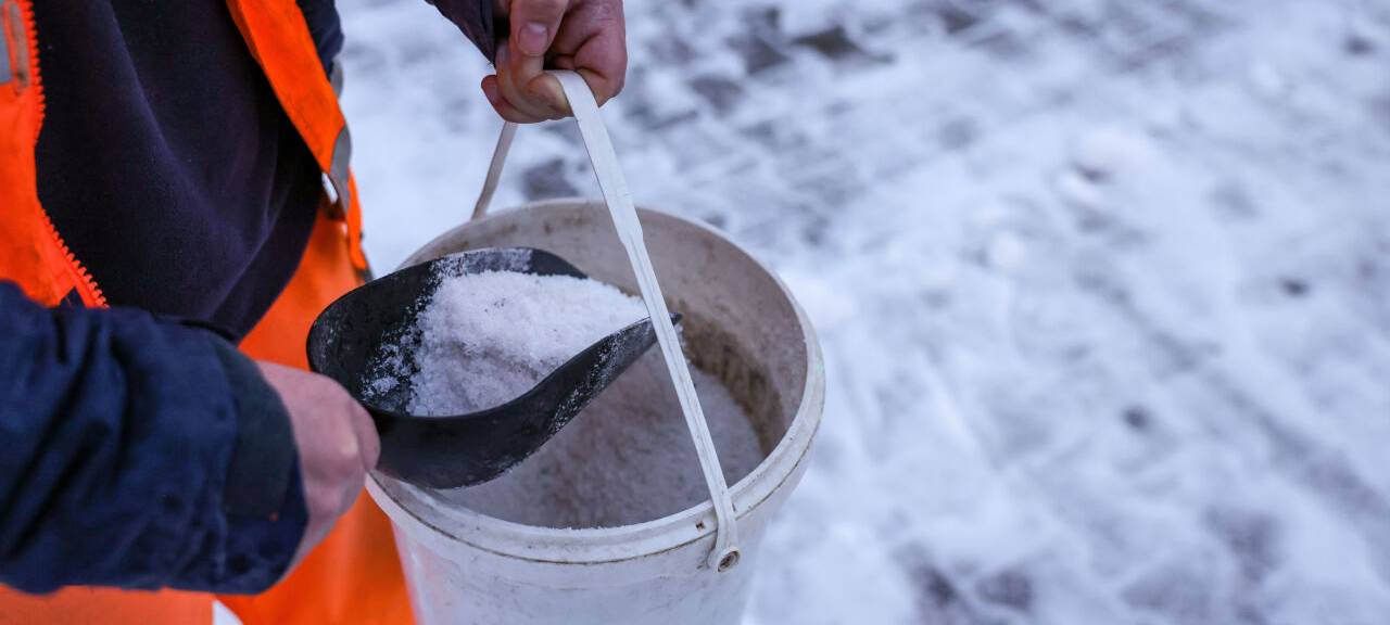 Ein Mitarbeiter des Winterdienstes verteilt Streusalz bei Regen und Schneeglätte auf den Fußweg an einer Straßenkreuzung.