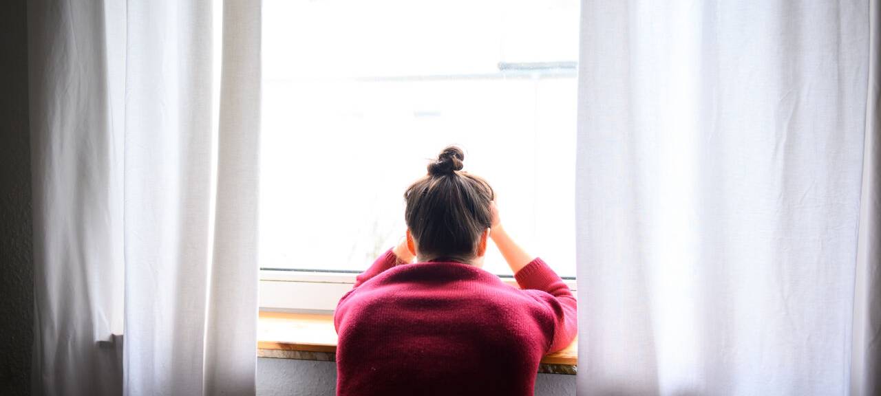Eine Frau sitzt mit Kopf in den Händen am Fenster