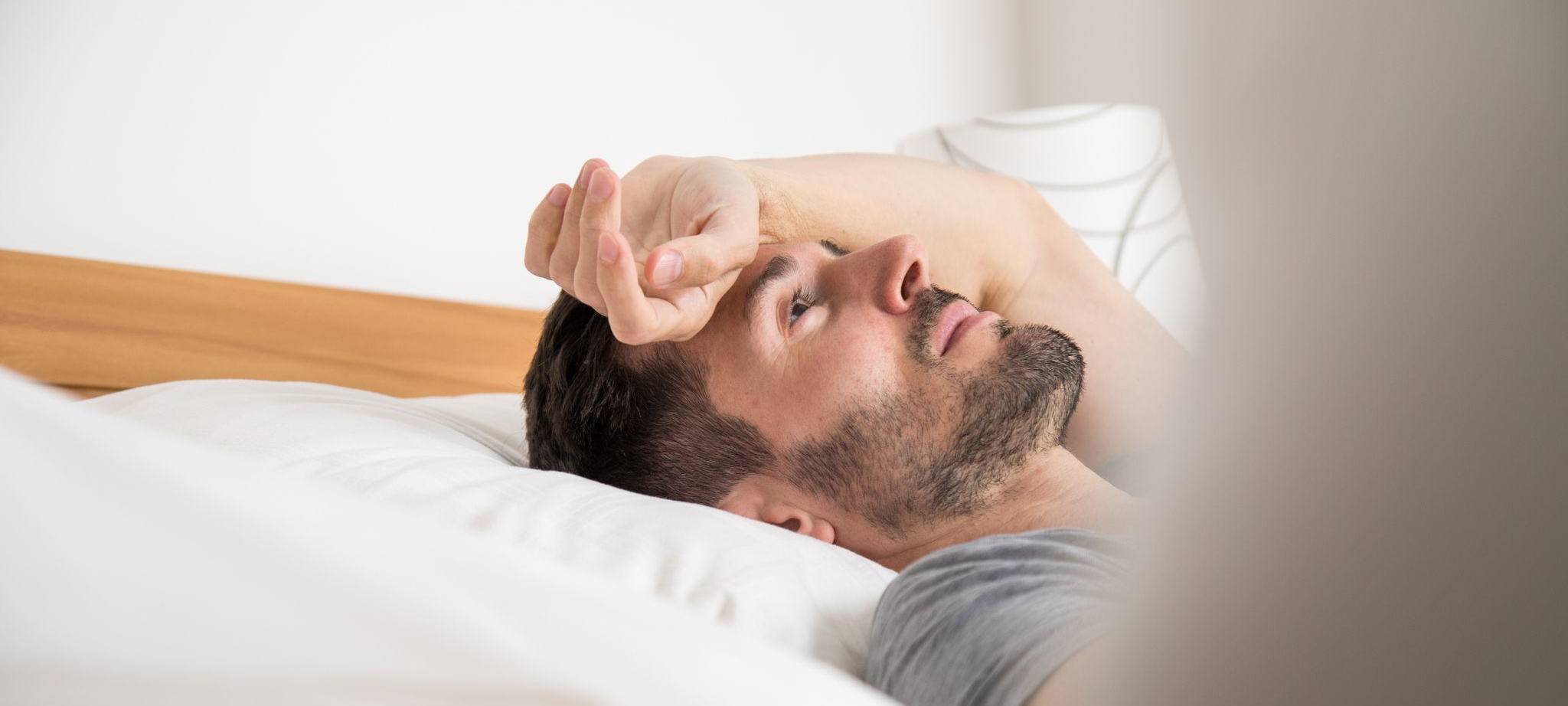 Mann liegt schlaflos im Bett