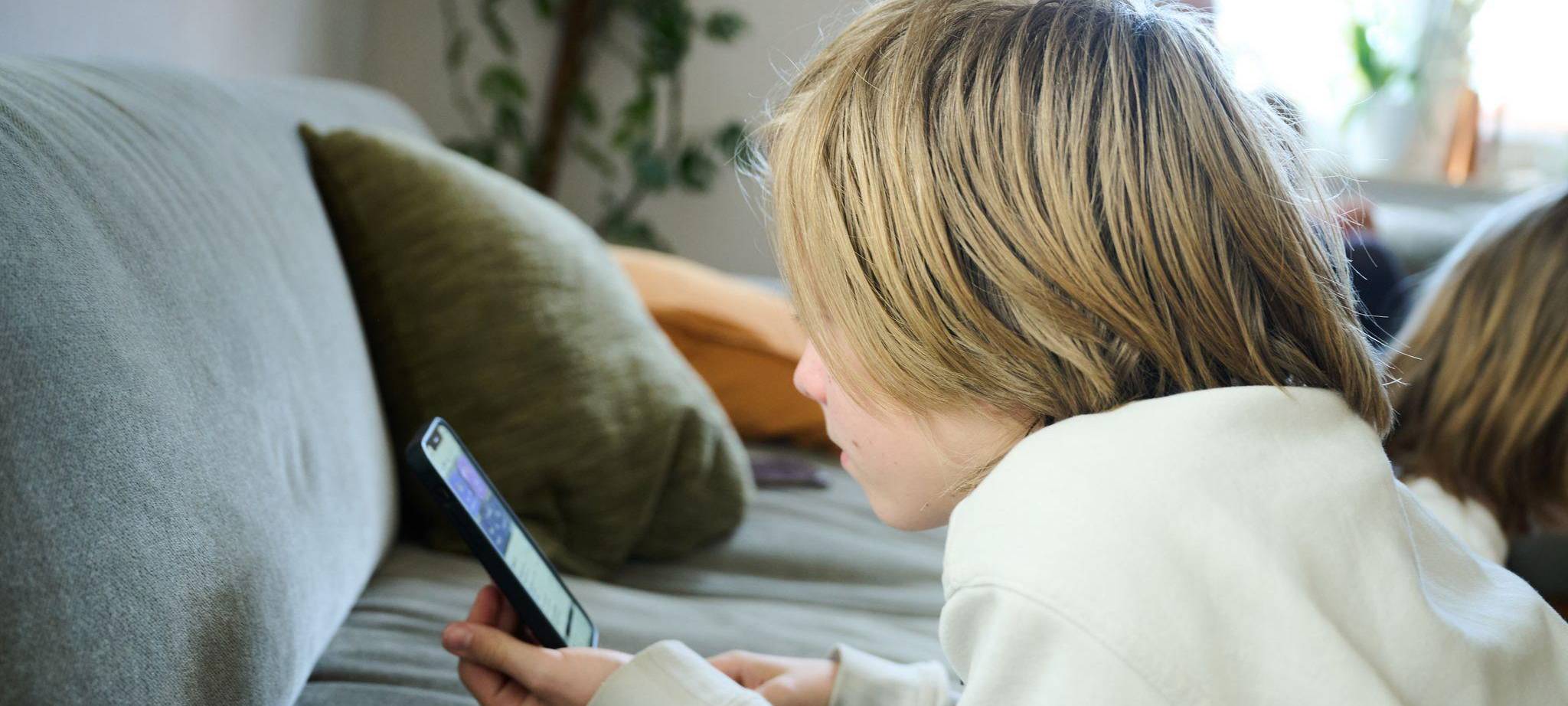 Ein Junge liegt auf einem Sofa und guckt auf sein Smartphone